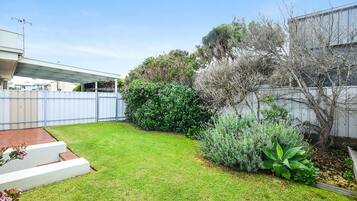 A well-maintained backyard with a grassy lawn, a small garden area with various plants, and a white fence.