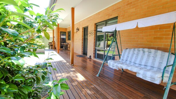 Una terraza de madera con una silla mecedora, un muro de ladrillo y una puerta de cristal que da a un patio.