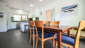 Un comedor con una mesa y sillas de madera, una cocina al fondo y un cuadro en la pared.