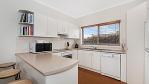 Eine moderne Küche mit weißen Schränken, einer Mikrowelle, einem Spülbecken und einem Fenster mit Jalousien.