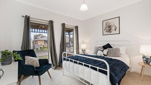 Ein Schlafzimmer mit Bett, Nachttischen, einem Sessel, einem Fenster und einer Pendelleuchte.
