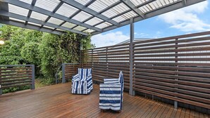 Eine Holzterrasse mit einem Metall-Pergola, zwei gestreiften Kissen und einem Tisch mit Überdachung.