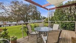 Un patio techado al aire libre con una mesa redonda y sillas, con vista a una marina con barcos y un área verde.