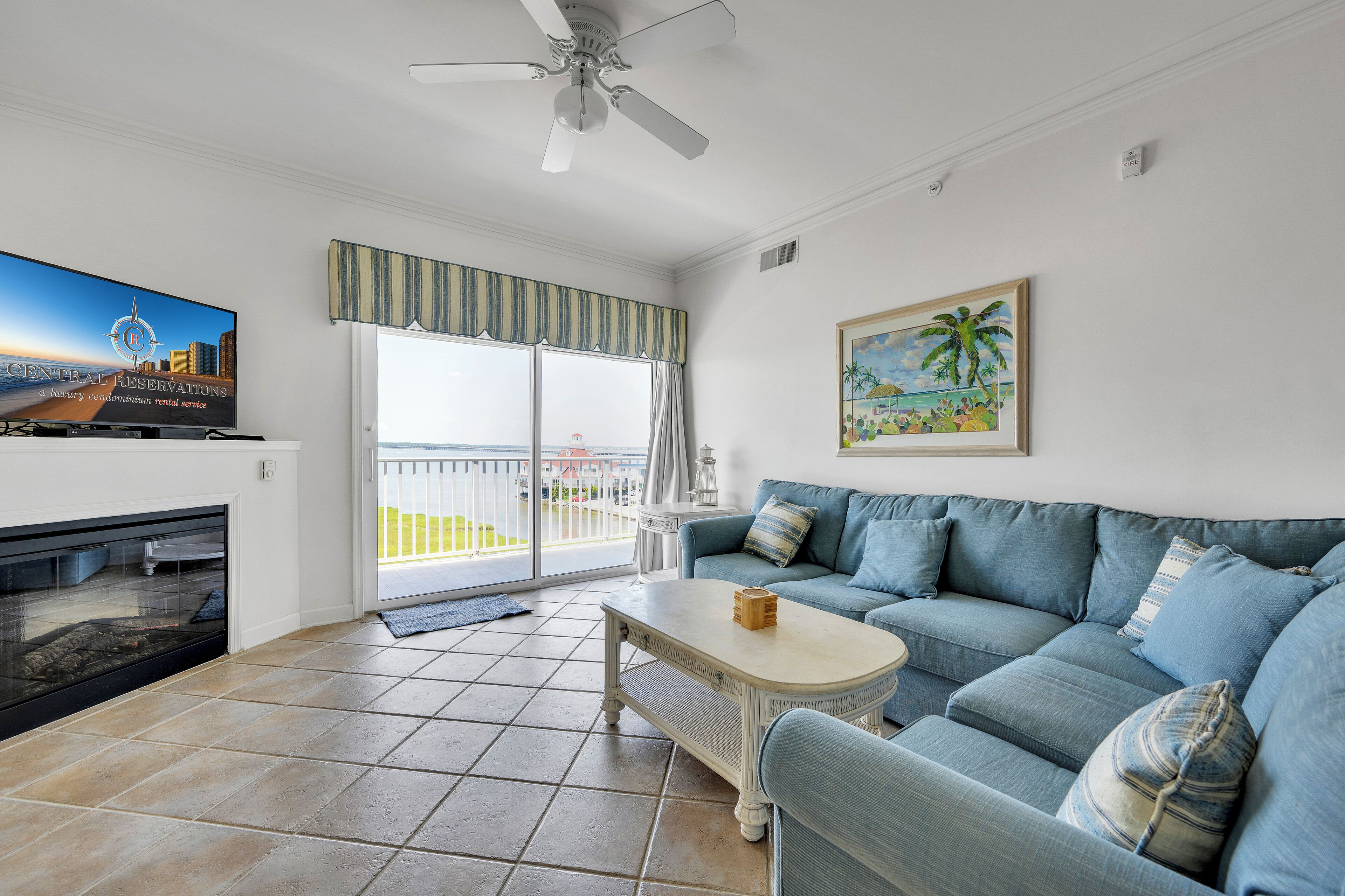 A living room with a TV, a sofa, a coffee table, a fireplace, and a balcony with a view.