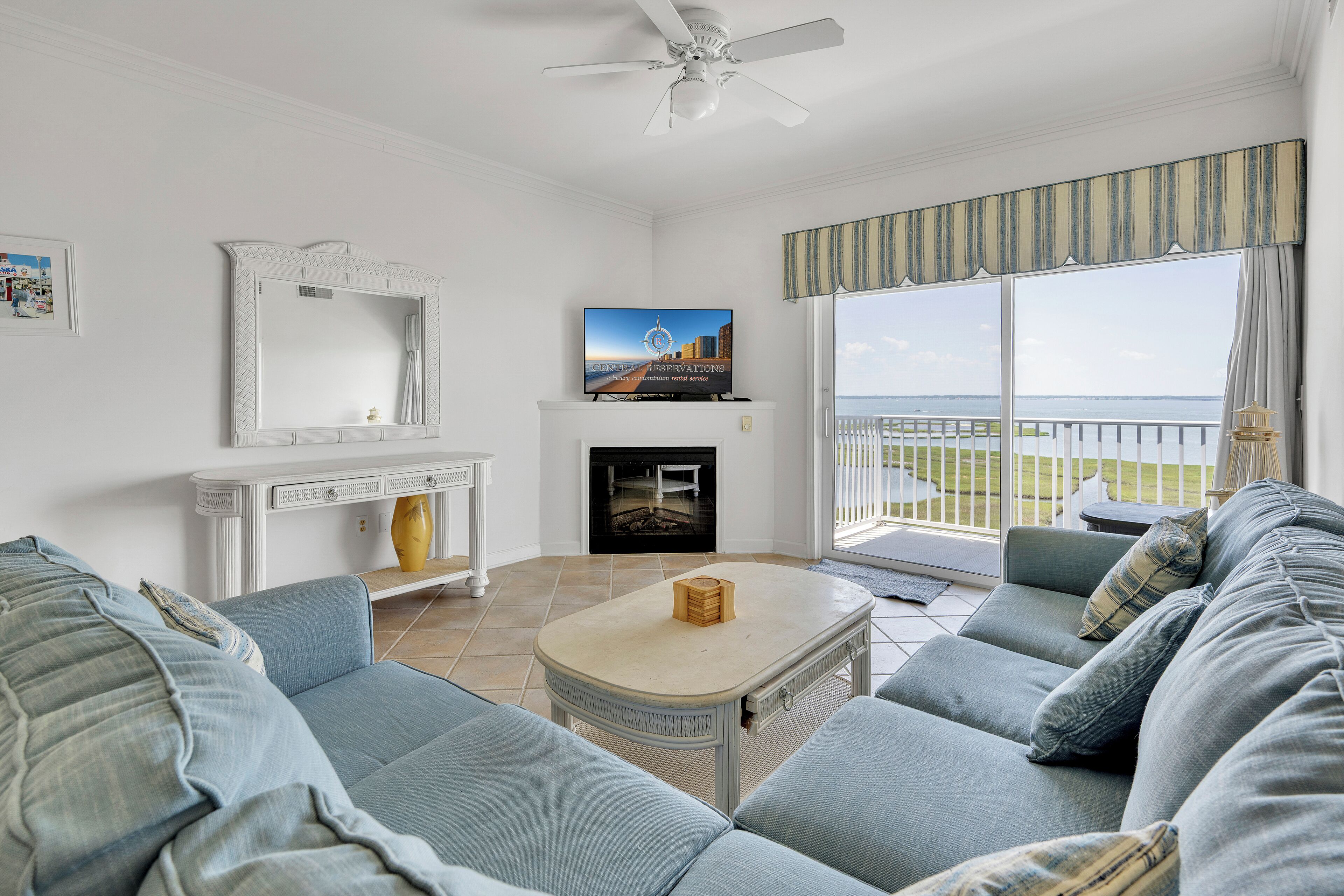 A living room with a sofa, a fireplace, a television, and a balcony with a view.