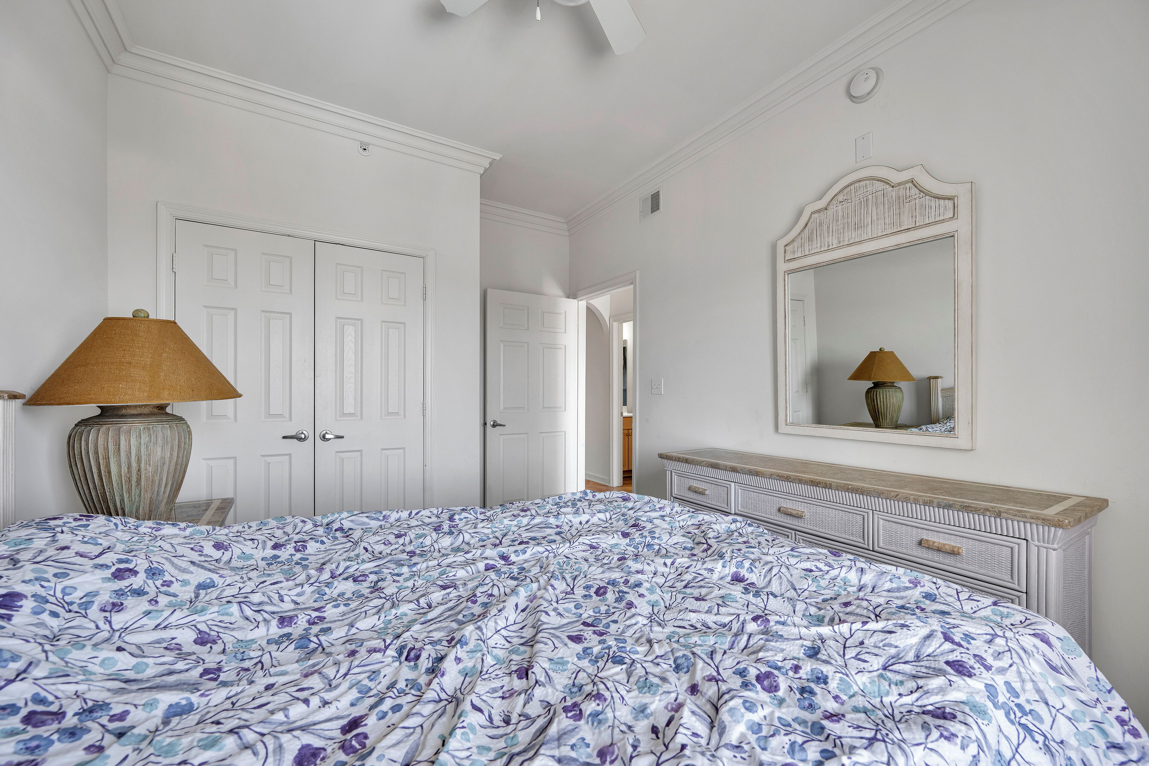 A bedroom with a large bed, a dresser, a lamp, and a mirror.