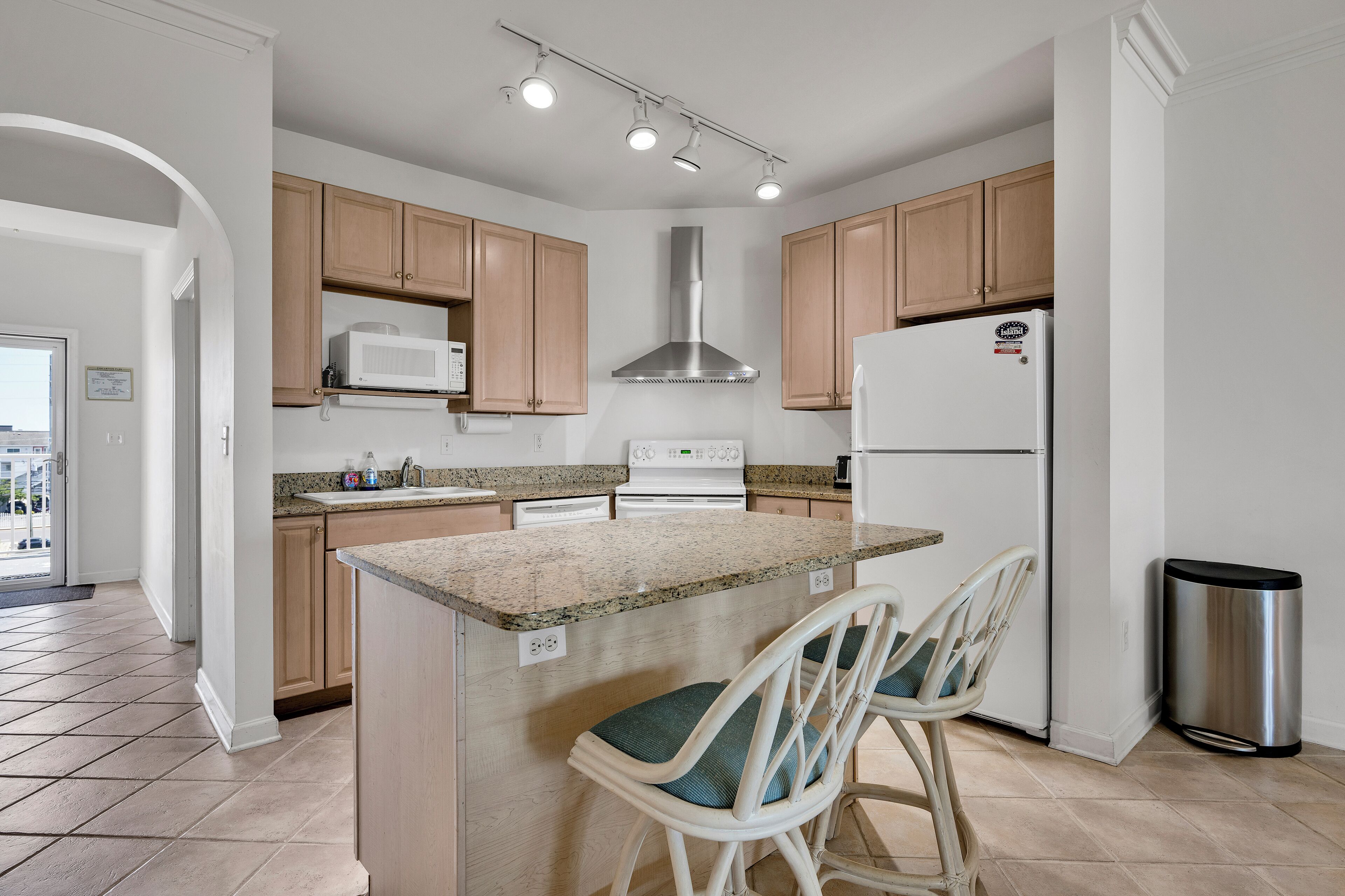 Cocina moderna con armarios de madera, extractor de acero inoxidable, microondas integrado y refrigerador de acero inoxidable. Hay una pequeña isla con dos taburetes de bar.
