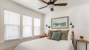 A bedroom with a large bed, a ceiling fan, and three windows with blinds. - Remodeled Designer Cottage with Bicycles (Culver City)