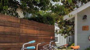 A row of bicycles parked in front of a building with a wooden fence and greenery in the background. - Remodeled Designer Cottage with Bicycles (Culver City)