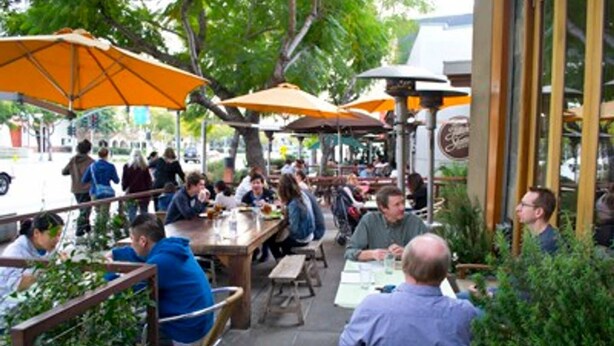 An outdoor dining area with tables and orange umbrellas. - Remodeled Designer Cottage with Bicycles (Culver City)