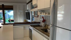 Una cocina moderna con armarios blancos, horno empotrado, refrigerador y ventana con vista a un jardín.