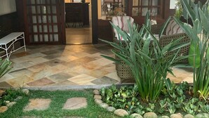Un espacio exterior cubierto con suelo de baldosas, una zona de estar con sofá y sillones, y una mesa de comedor.