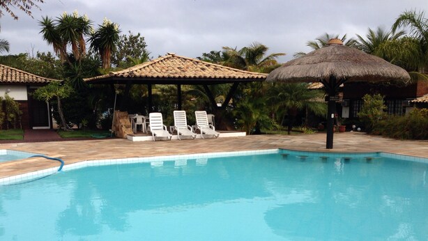 Una piscina con sillas de descanso y una estructura de techo de paja.
