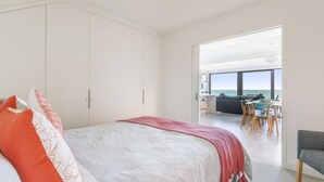 A bedroom with a bed, a wardrobe, and a view of a dining area with a table and chairs. - Aqua Mist Seascape - refreshing ocean-views (Port Fairy)