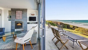 A modern living room with a fireplace, TV, and seating area overlooking a beach. - Aqua Mist Seascape - refreshing ocean-views (Port Fairy)