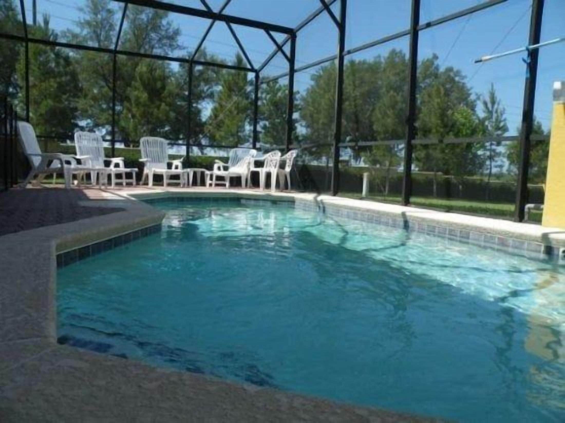 Een zwembad met helder water, omringd door een overdekt terras met stoelen.