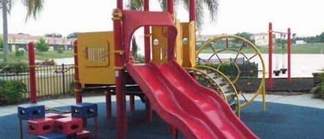 A playground with a red slide and yellow and red play structures.