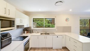 A modern kitchen with white cabinetry, a built-in oven, a microwave, a dishwasher, and a window with a view of greenery.