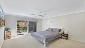 A bedroom with a bed, a ceiling fan, a clock, and a view of the outside through a sliding door.