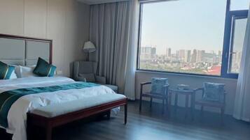 A hotel room with a large bed, a desk, two chairs, and a view of a cityscape.