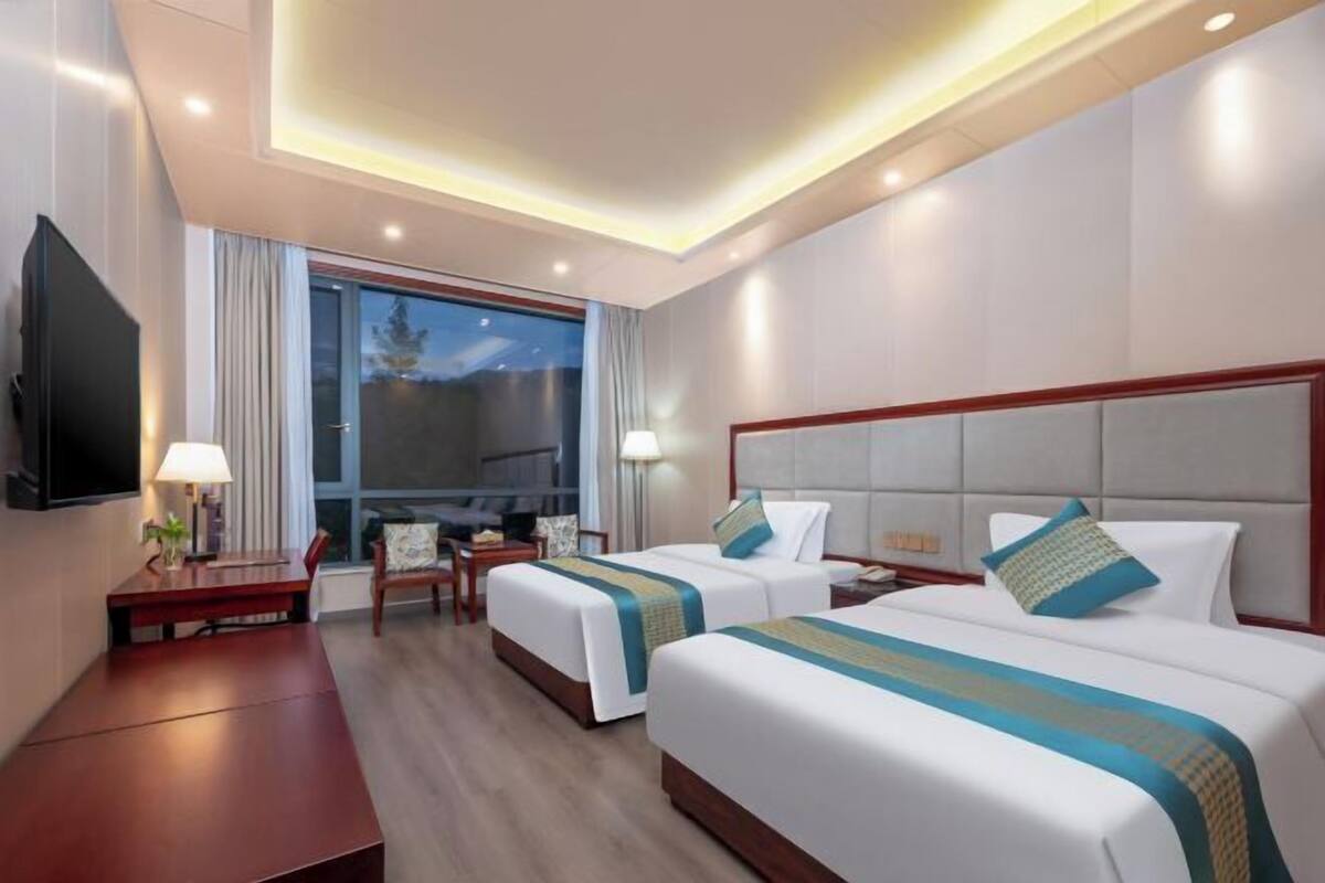 A hotel room with two beds, a TV, a desk, and a window with curtains.