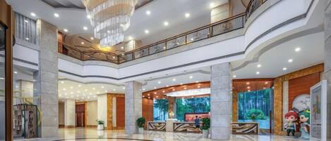 A spacious lobby with a central circular area, a grand chandelier, and a second-floor balcony.