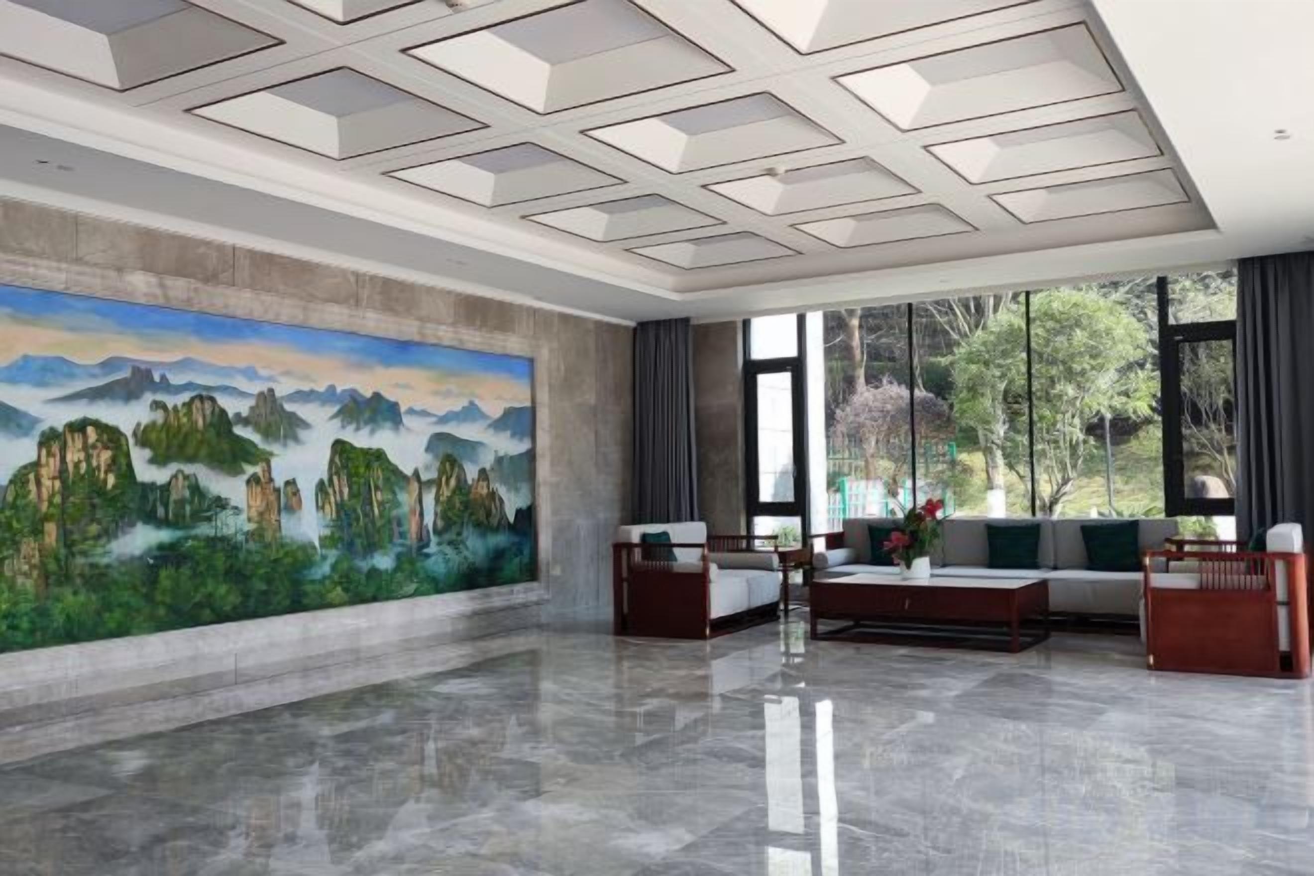 A spacious lobby with a large mural, modern furniture, and large windows offering a view of greenery.