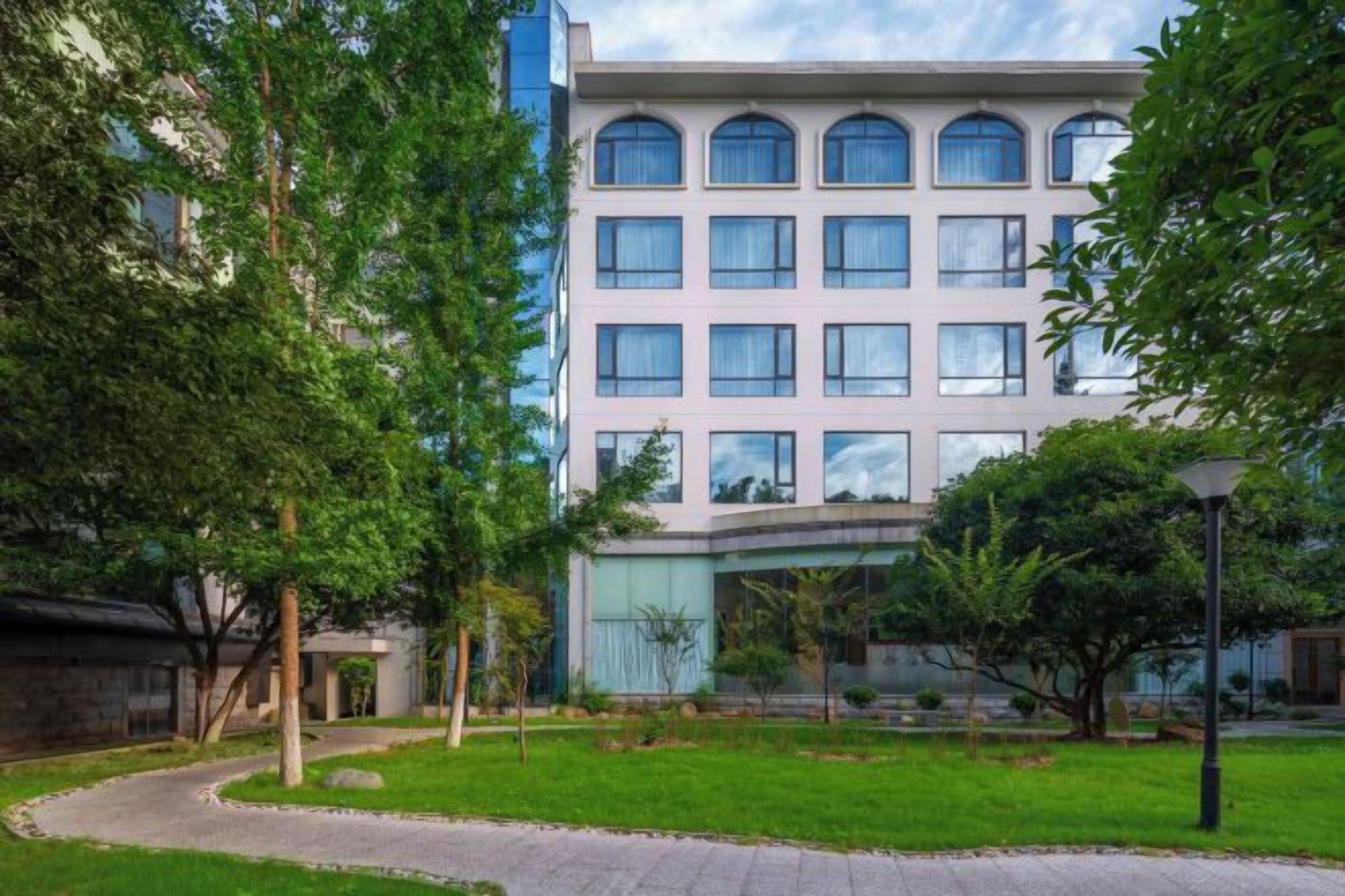 A multi-story building with a central courtyard, surrounded by trees and a paved walkway.
