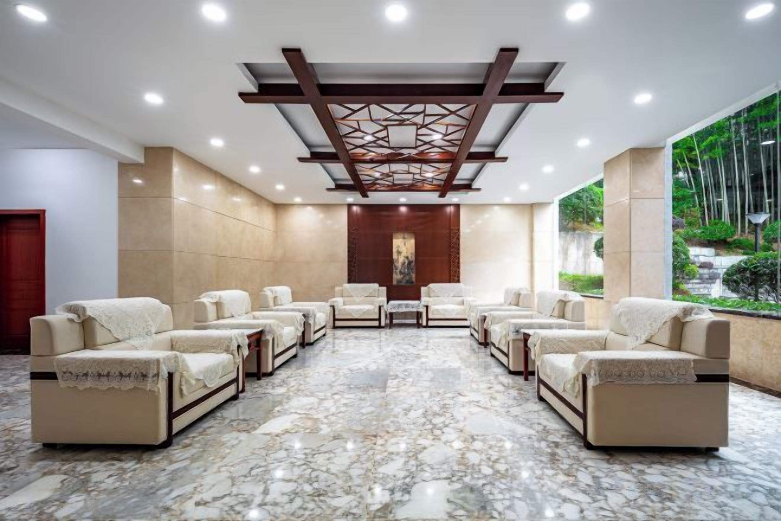 A hotel lobby with a marble floor, multiple sofas arranged in a semi-circle, and a large window offering a view of greenery.