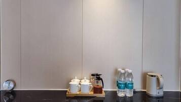 Une chambre d’hôtel avec un comptoir en marbre, une machine à café, deux tasses, un plateau avec une théière et deux bouteilles d’eau.