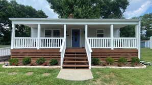 A two-story house with a front porch, a blue door, and a small front yard with red flowers.
