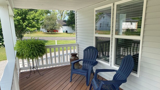 A porch with two blue Adirondack chairs, a potted plant, and a view of a white house in the background.