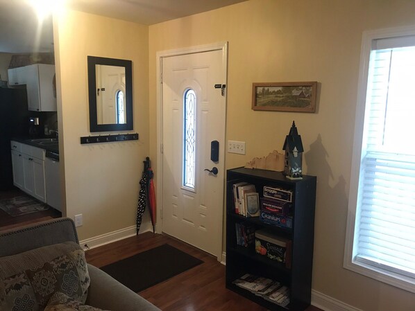 A living room with a sofa, a bookshelf with books and decorative items, a door with a window, and a kitchen area in the background. - Waterworks come to relax (Williamstown)