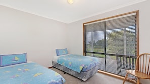 Two single beds with nautical-themed bedspreads, a wooden chair, and a large window with horizontal blinds.