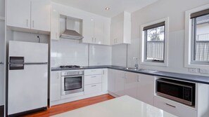 A modern kitchen with white cabinets, a stainless steel refrigerator, a built-in oven, a microwave, and a window providing natural light. - Stenmark - 5/3 Poley Cow Lane (Jindabyne)