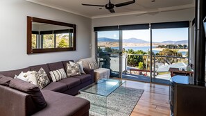 Relax in this stylish living room with a large sofa, glass coffee table, and scenic views of the coastal landscape through the sliding glass door.