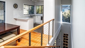 A modern kitchen with a central island, white cabinetry, and a dining area with a wooden table and bench. - Aspect - 2/8a Poley Cow Lane (Jindabyne)