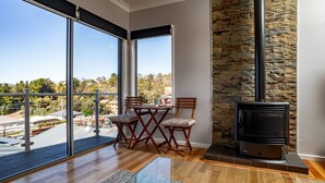 A balcony with a stone wall, a fireplace, and a view of the surrounding area. - Aspect - 2/8a Poley Cow Lane (Jindabyne)