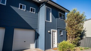 A two-story residential building with a garage, a front door, and a small window. - Aspect - 2/8a Poley Cow Lane (Jindabyne)