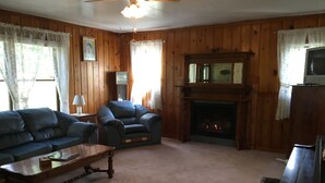 Una sala de estar acogedora con paneles de madera, una chimenea, un sofá, un sillón reclinable y un televisor.