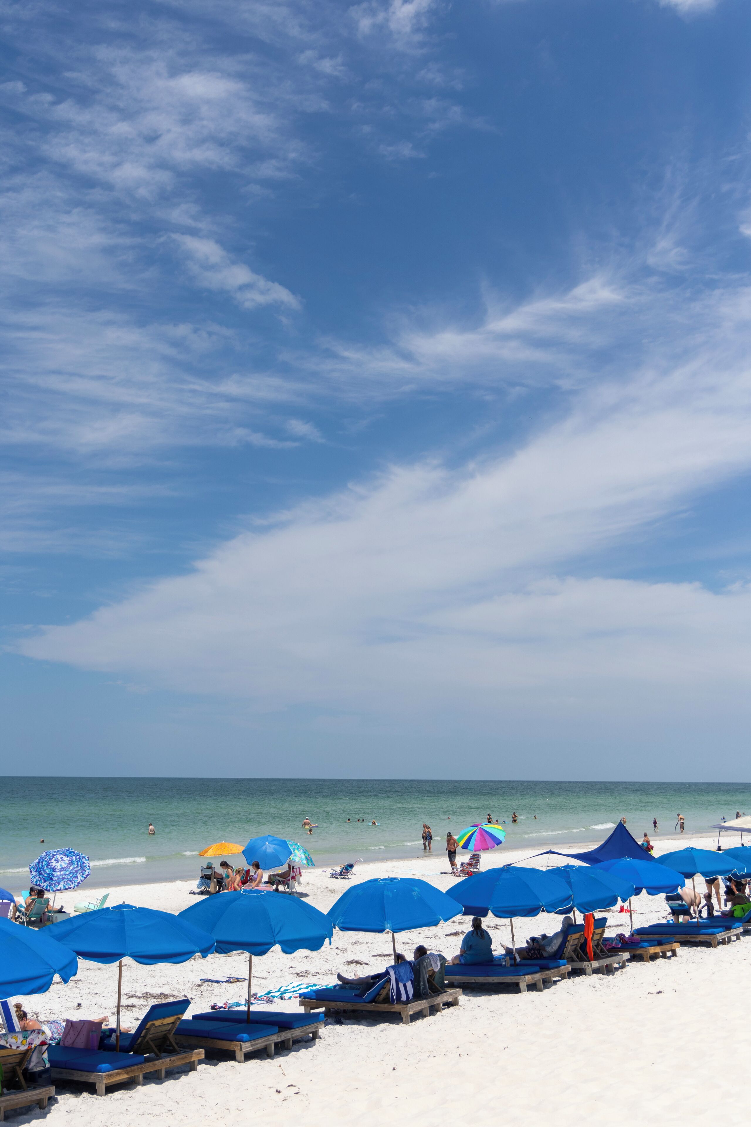 Ein Strand mit Reihen blauer Sonnenschirme und Liegestühle, ein klarer Himmel und das Meer im Hintergrund.