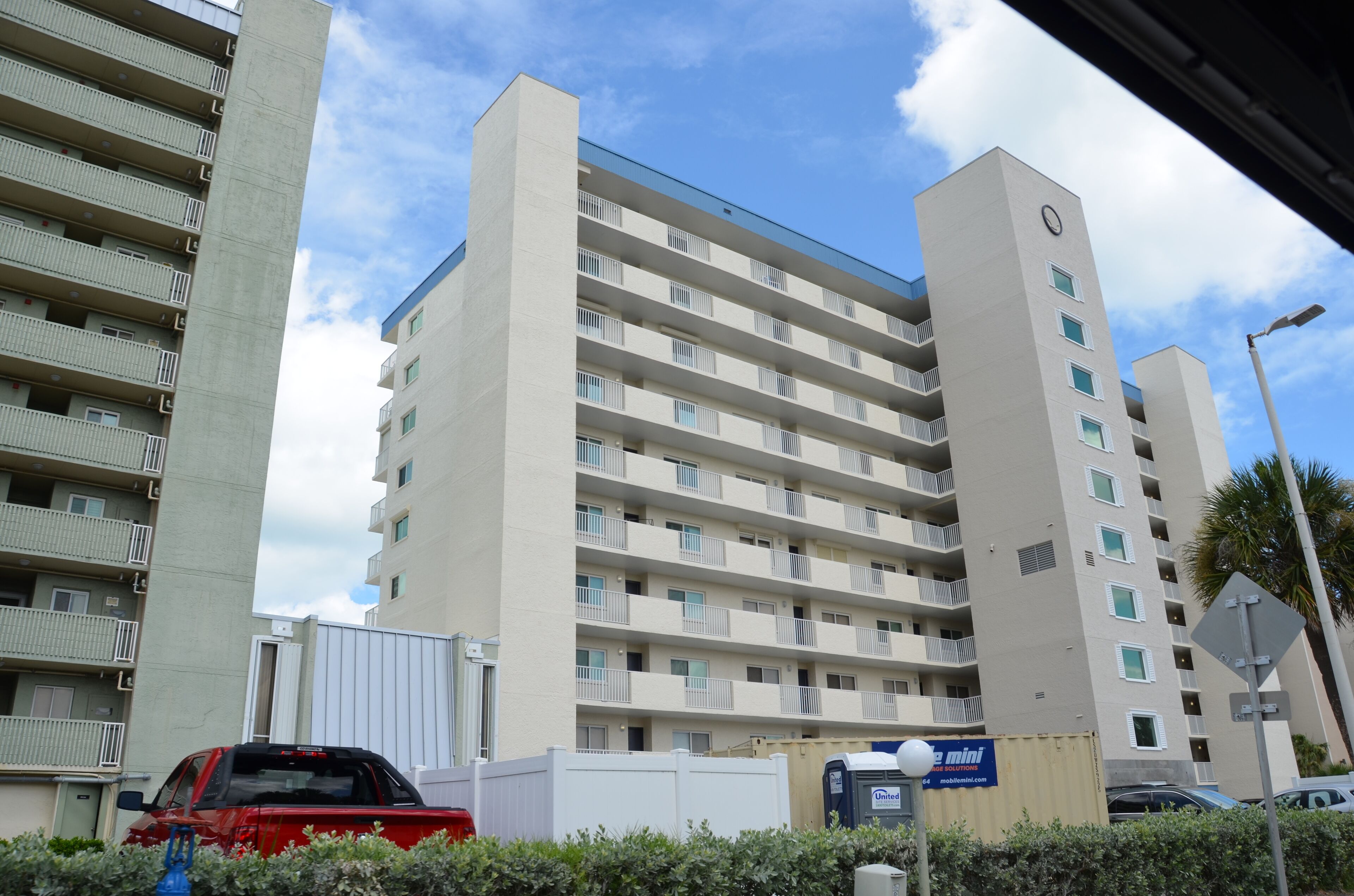 A multi-story building with balconies, a clock on the side, and a visible street sign.