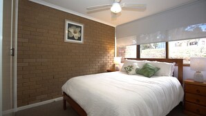 A bedroom with a brick wall, a ceiling fan, a window with a view, and a bed with pillows.