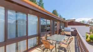 En overdækket terrasse med glasvægge, udendørs møbler og grill.