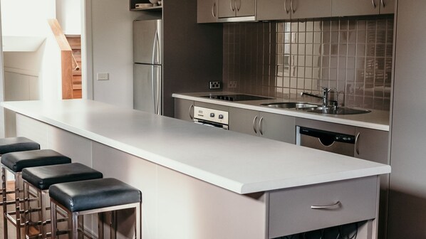 A modern kitchen with a white countertop, stainless steel appliances, and a tiled backsplash. - Castwood Villa 1 - Overlooking the Gardens Oval & Botanic Gardens (Port Fairy)