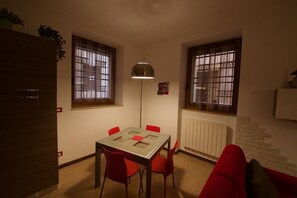A small dining area with a glass table, red chairs, a floor lamp, and barred windows. - Marconi Rooms - Porta Leoni Suite (Verona)