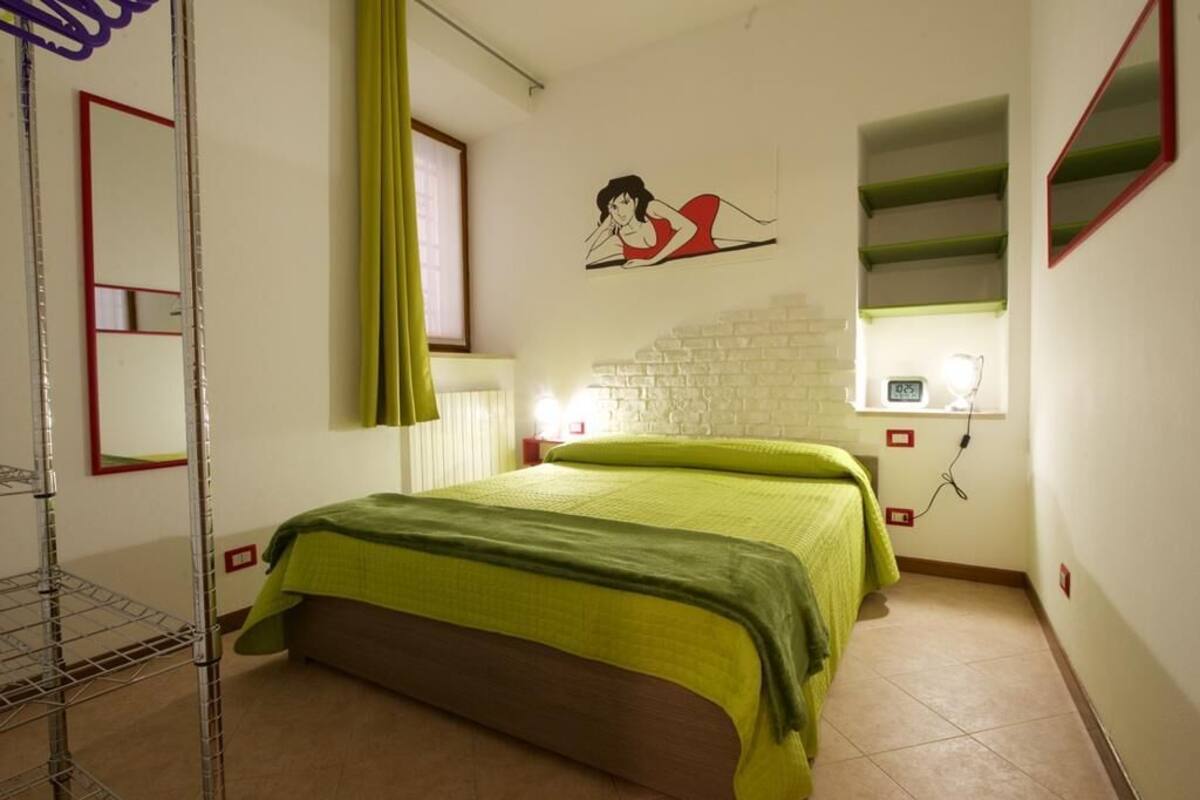 A bedroom with a bed, a green curtain, a wall clock, and a shelf with a mirror.