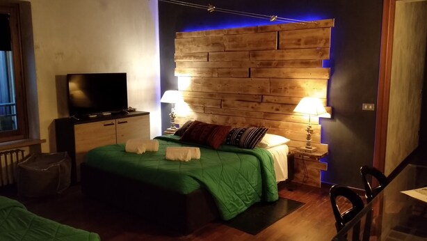 Un dormitori modern amb un panell de fusta al capçal, un televisor de pantalla plana, un llençol de llit verd i dues làmpades laterals.