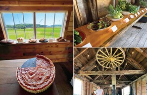 A rustic wooden cabin with a large window overlooking a field, a wooden table with a pie and bread, and a ceiling with a decorative wheel. - Harbor views + stylish interior + boat lounge (Beals)