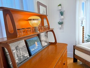 Un buffet en bois surmonté d’une lampe en verre, avec des livres et un plateau de verres.